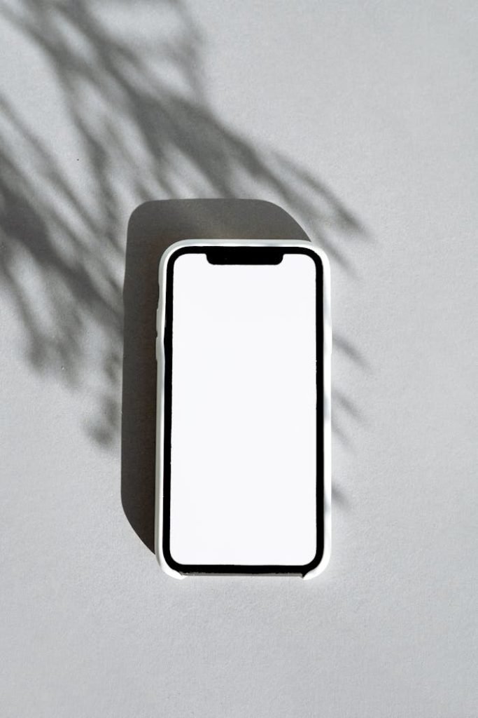 Blank smartphone screen on gray background with artistic leaf shadow.